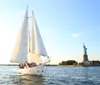 A sailboat is gliding across the water near the Statue of Liberty during a beautiful sunset