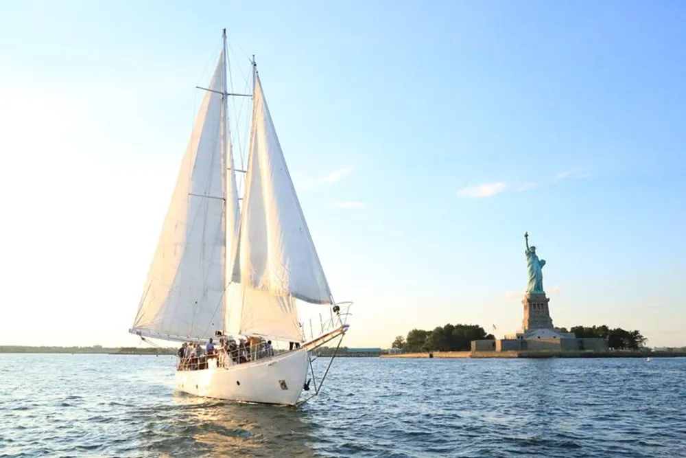 A sailboat glides through the water near the Statue of Liberty under a clear sky