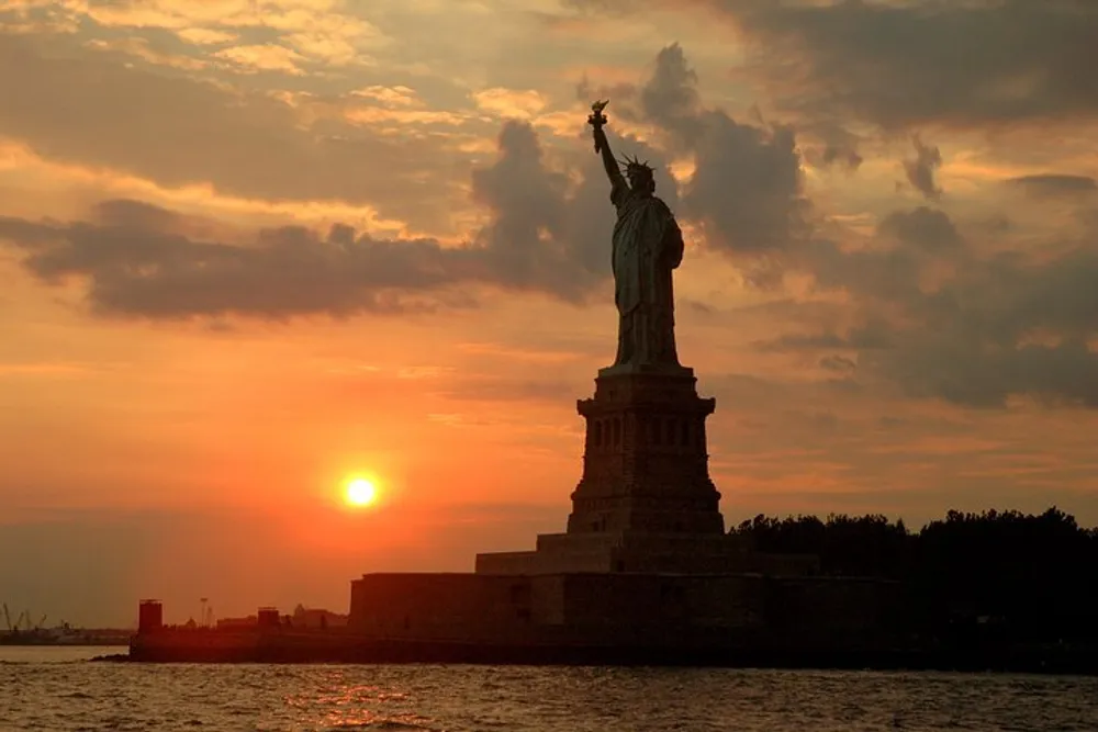 The Statue of Liberty is silhouetted against a stunning sunset sky