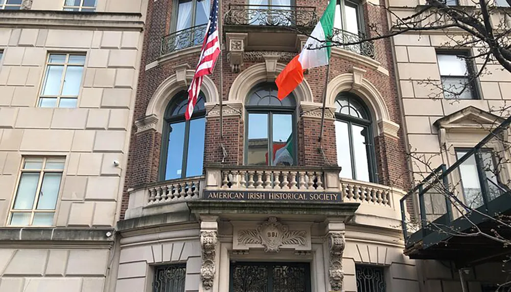 The image shows the facade of the American Irish Historical Society building with American and Irish flags hanging above a balcony adorned with the organizations name