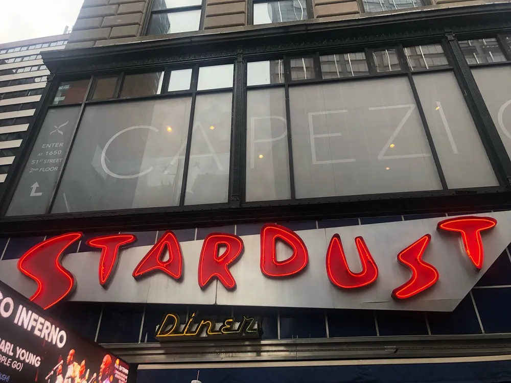 The image shows the exterior of a building with a neon sign that reads STARDUST in bright red with a partially visible sign reading Diner beneath it