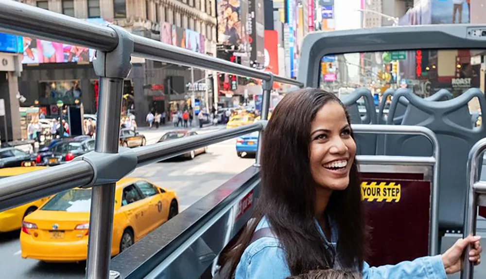 A smiling woman is enjoying a sightseeing bus tour in a bustling cityscape filled with yellow taxis and vibrant billboards