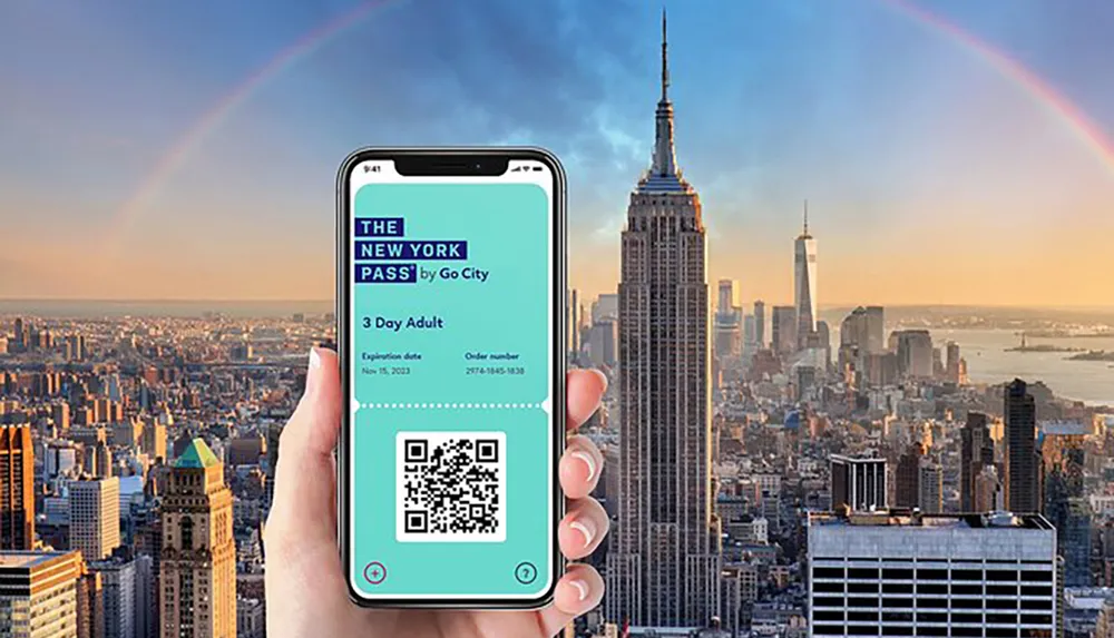 A hand holds up a smartphone displaying a New York Pass ticket with a QR code in front of a panoramic view of New York City