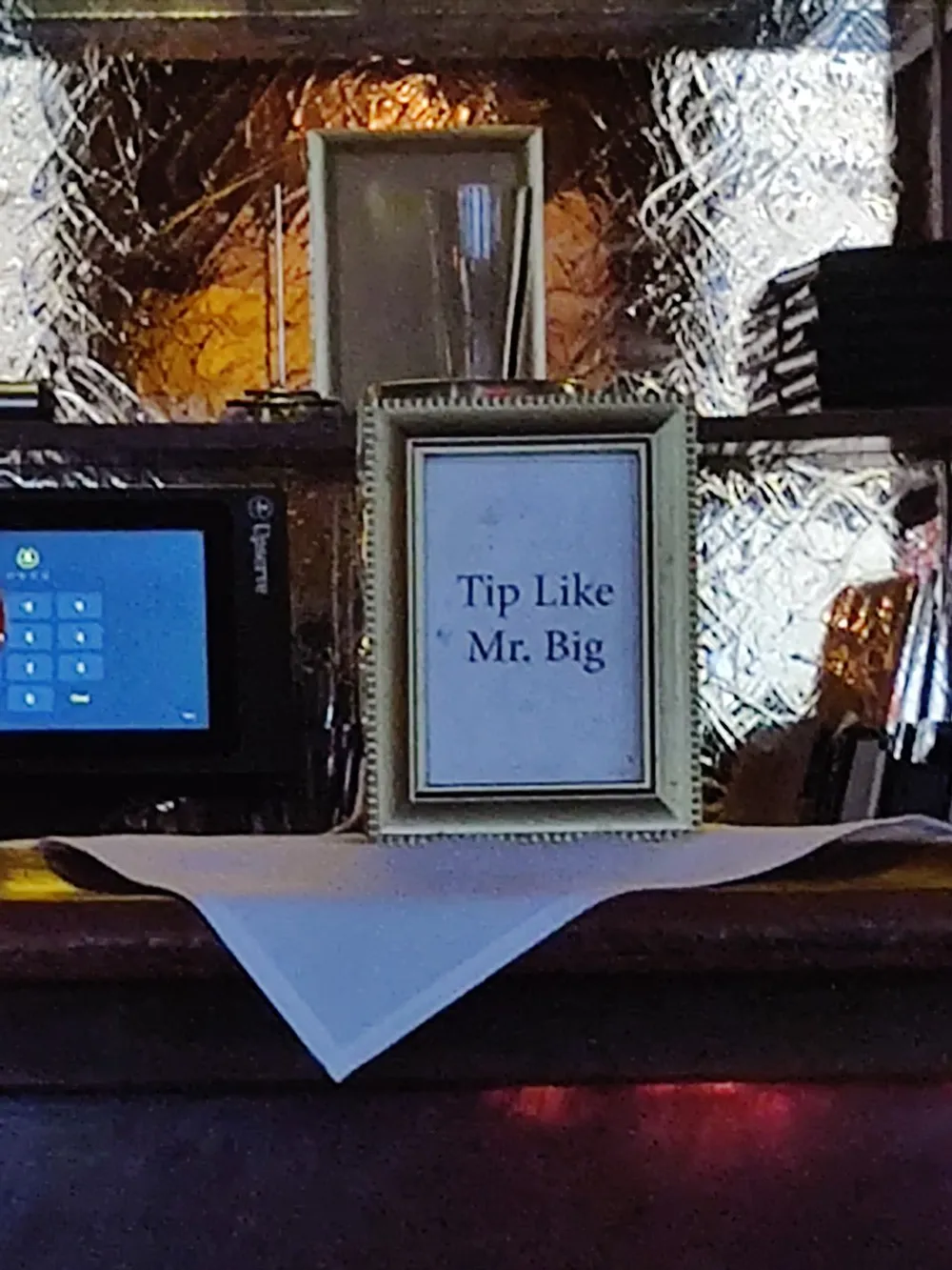 The image shows a sign placed on a counter with the words Tip Like Mr Big suggesting customers should leave generous tips