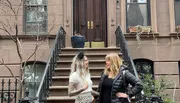 Two individuals are engaging in a pleasant conversation on the steps of a classic brownstone building.