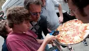 A group of people is focused on measuring a large pizza using a digital caliper.