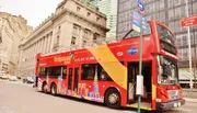 A red double-decker sightseeing bus is parked on a city street with buildings and a 