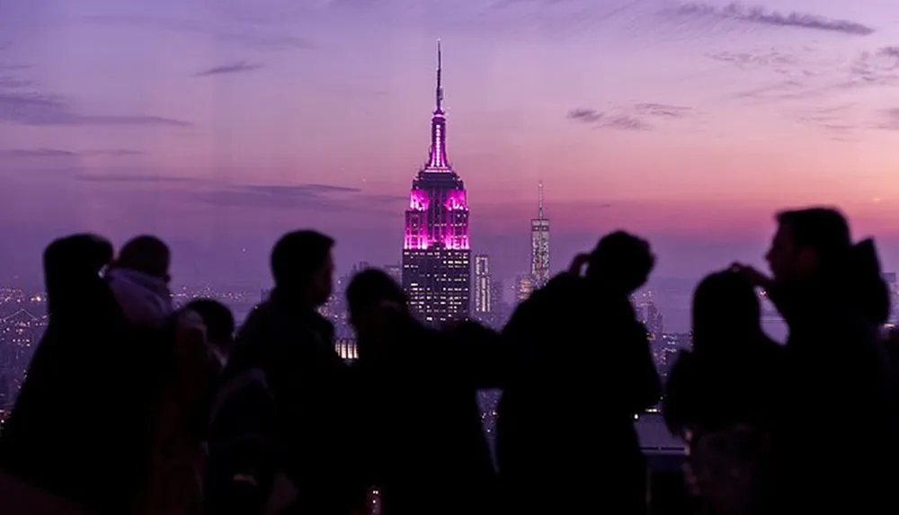 Silhouettes of people are gathered against a dusky skyline featuring an illuminated Empire State Building