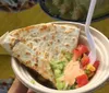 A person is holding a plate with a quesadilla and toppings of guacamole salsa and a spoonful of cream or cheese