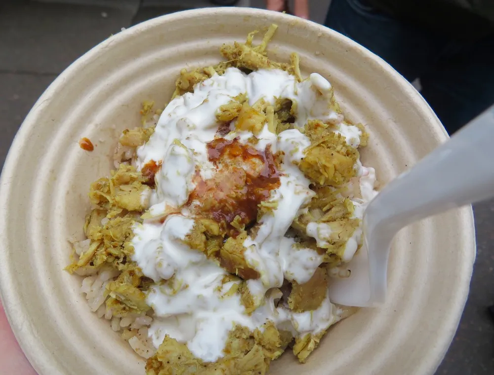 The image shows a close-up of a dish with rice seasoned meat a creamy sauce and possibly some herbs served in an eco-friendly disposable bowl with a plastic fork