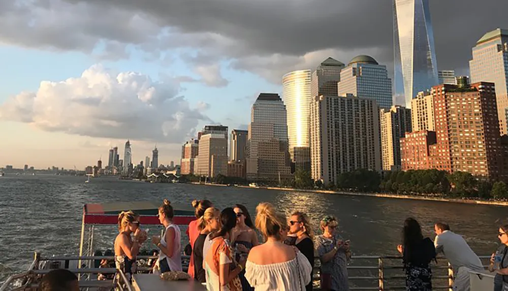 A group of people are enjoying a boat cruise with a view of a gleaming skyline bathed in the golden light of the setting sun