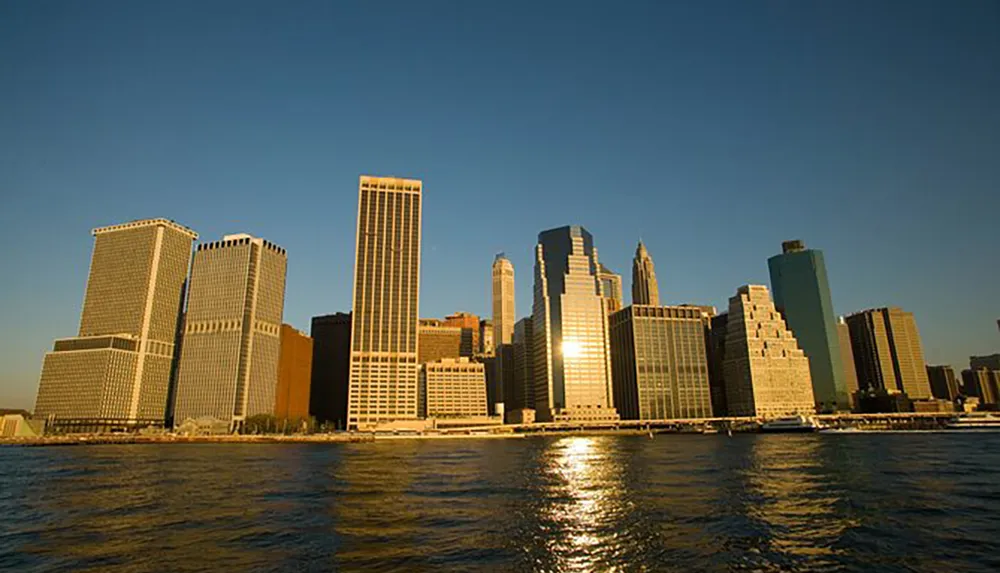 The image showcases a sunset view of a city skyline across the water reflecting golden hues on the skyscrapers facades