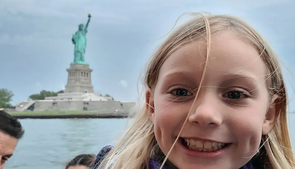 A joyful young child is posing for a photo with the Statue of Liberty in the background