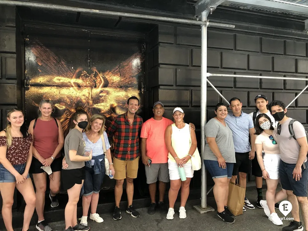 A group of eleven people are smiling for a photo in front of a dark wall featuring a shiny embossed artwork of what appears to be a mythical creature possibly a dragon