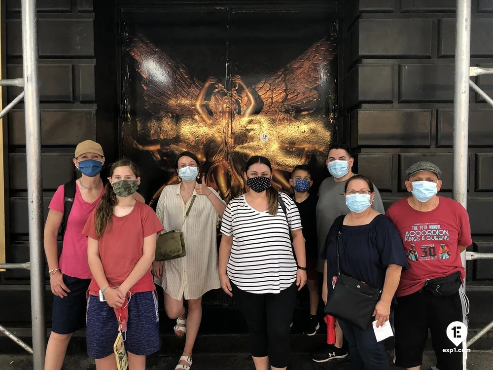 A group of people wearing protective face masks are posing for a photo in front of an ornate door with a striking golden insect design