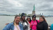 A group of people is posing for a photo with the Statue of Liberty in the background, suggesting they are tourists enjoying a visit to an iconic landmark.
