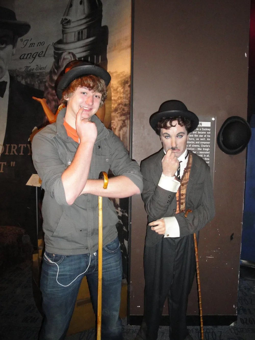 A person is posing with a lifelike figure of Charlie Chaplin mirroring the figures thoughtful hand gesture and wearing a similar hat