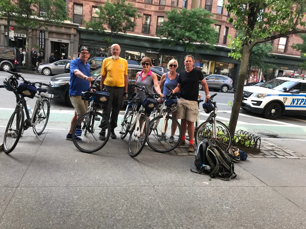 Four people with bicycles are standing on a city sidewalk possibly taking a break from cycling with a police vehicle visible in the background