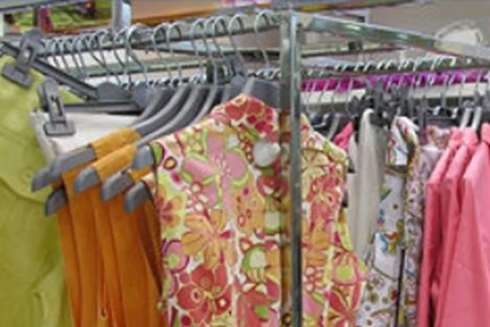 Colorful clothing items are displayed on racks in a store possibly a thrift shop given the variety and style of garments