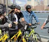 A group of cyclists wearing helmets pauses during a bike tour to listen to their guide with a city skyline and water as the backdrop