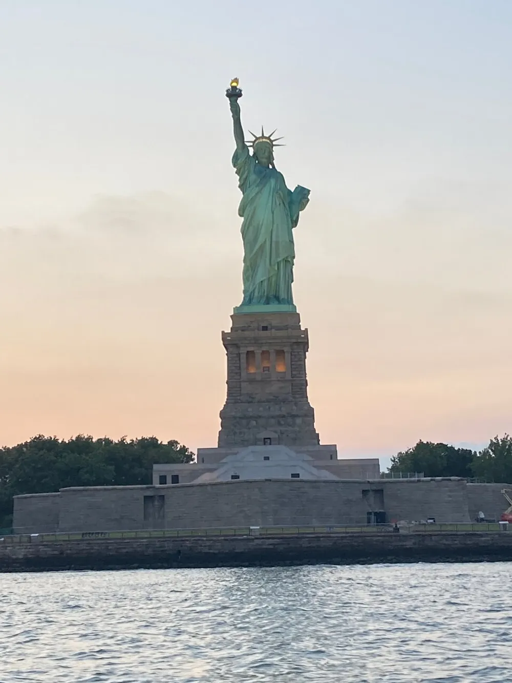 The Statue of Liberty stands tall against a dusky sky symbolizing freedom and welcoming visitors at a waterfront location
