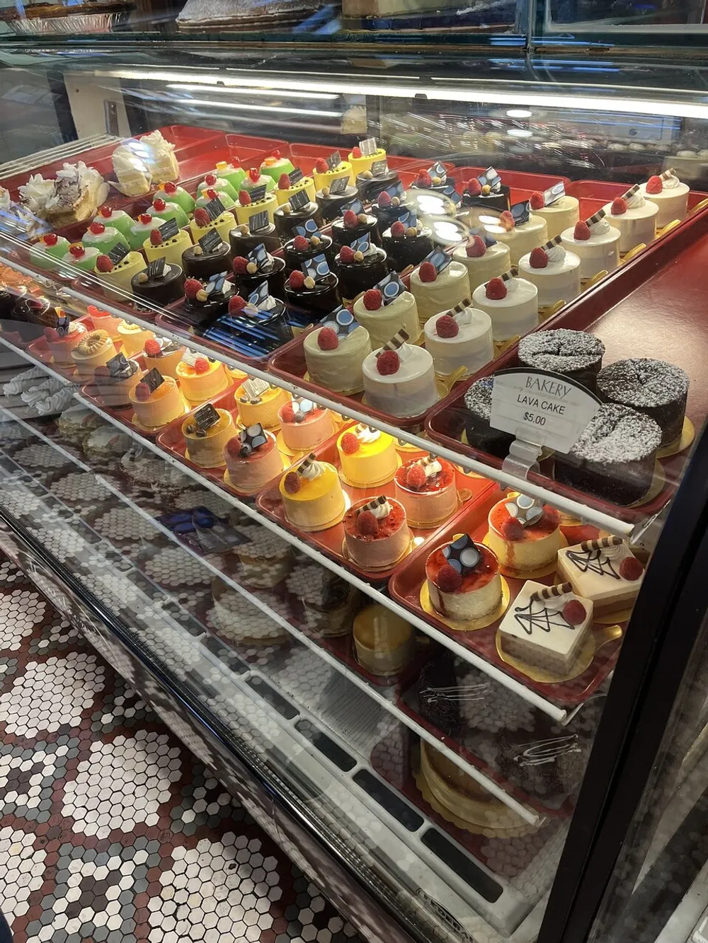A bakery display case filled with an array of colorful and tempting individual desserts including cakes and tarts topped with fruit and decorative elements