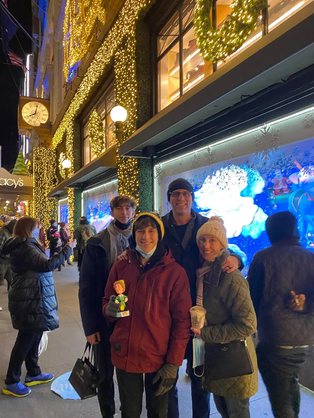 A group of people poses for a photo in front of a festively decorated storefront with Christmas lighting and window displays