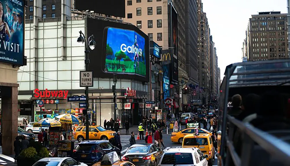 The image captures a busy urban street scene with taxis pedestrians a subway entrance and large advertisements likely in a major city like New York