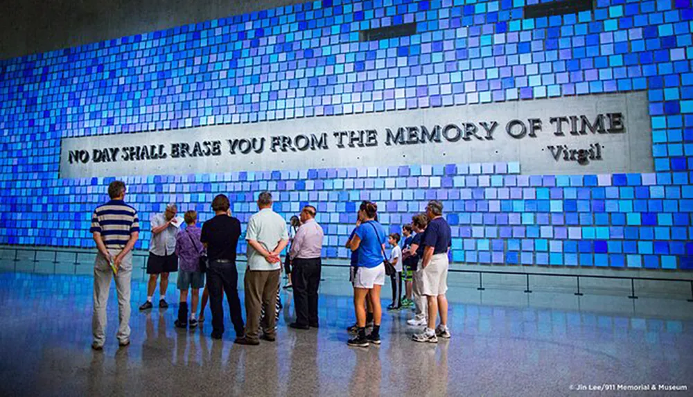 Visitors are viewing a large blue tile art installation with the inscription NO DAY SHALL ERASE YOU FROM THE MEMORY OF TIME Virgil at a museum or memorial