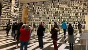 Visitors are observing an art installation with bold, black-and-white patterned floors and walls covered in large, thought-provoking text.