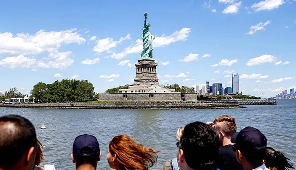 Tourists on a boat admire the Statue of Liberty against a backdrop of blue skies and the New York City skyline