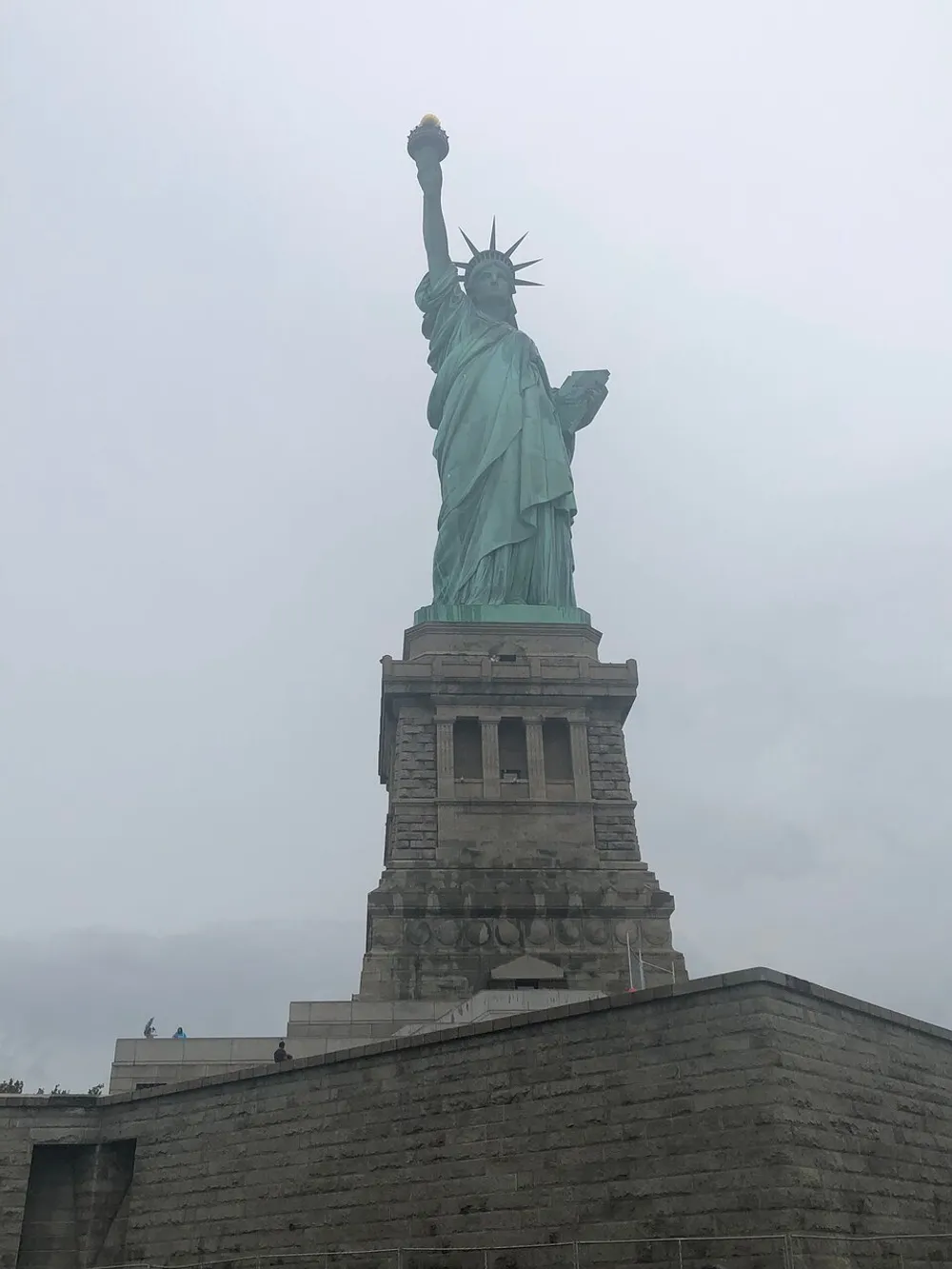The image shows the Statue of Liberty standing tall under an overcast sky
