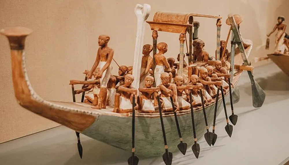 The image shows an intricately detailed ancient Egyptian funerary model of a wooden boat with rowers which was intended for the tomb of a noble or pharaoh to provide for the afterlife