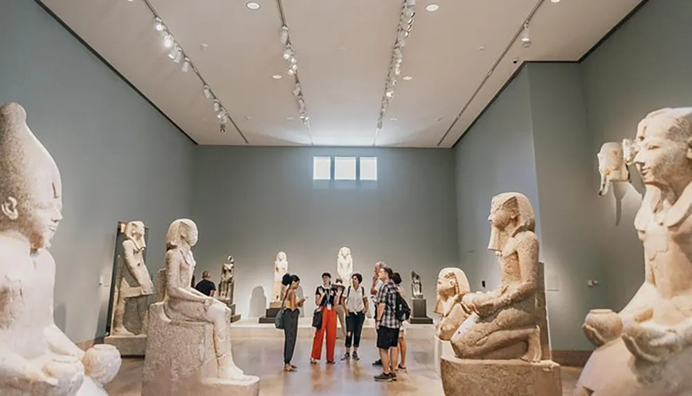 A group of visitors is observing ancient sculptures in a well-lit art gallery