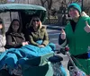 Three passengers are enjoying a festive pedicab ride with a driver dressed in a holiday-themed outfit giving a thumbs-up gesture