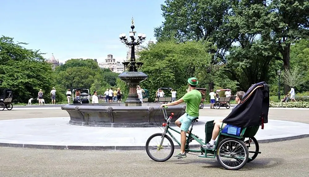 A pedicab driver pedals past a fountain in a lush city park with pedestrians in the background