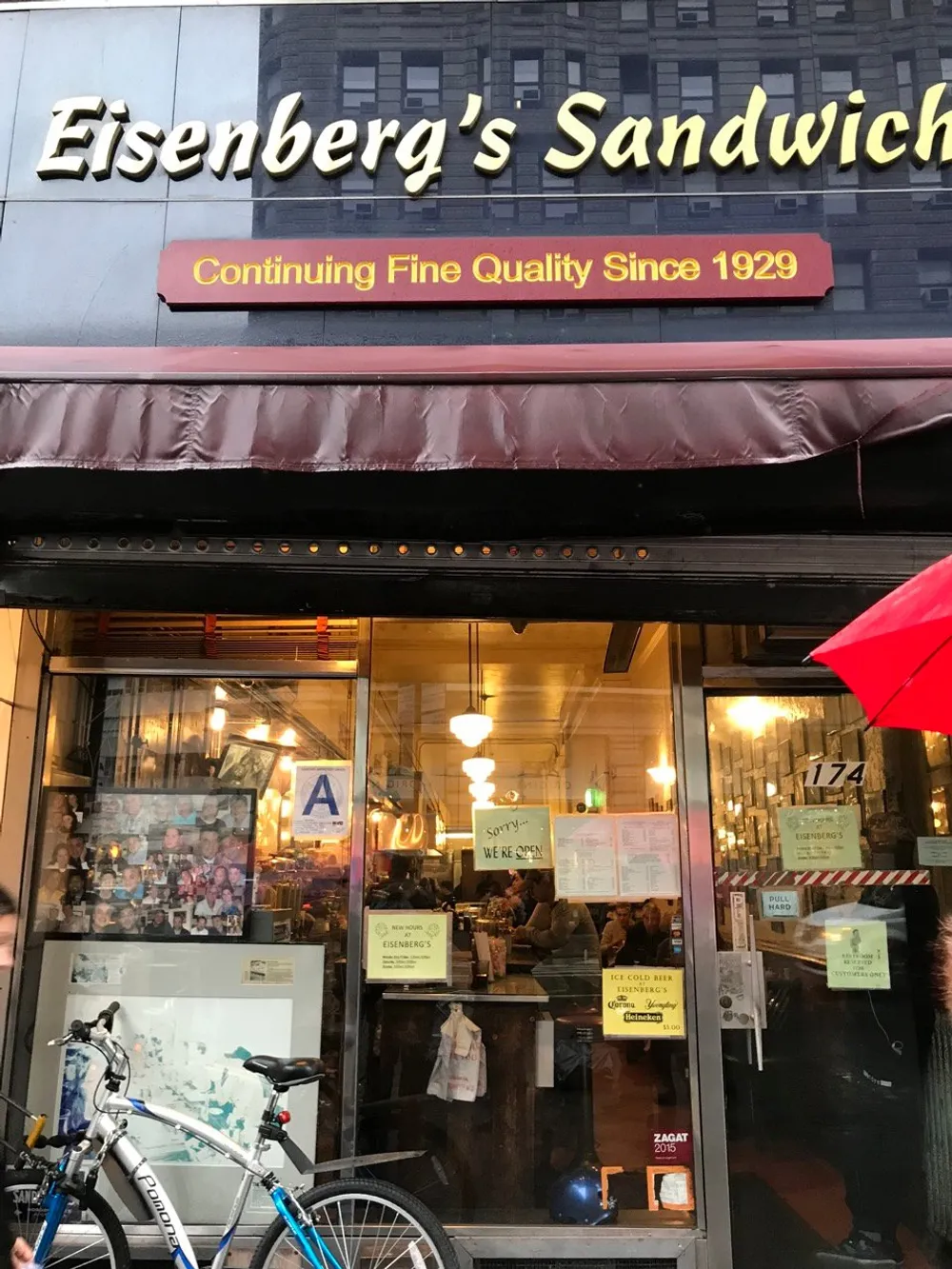 The image shows the front of Eisenbergs Sandwich Shop a restaurant with a classic storefront boasting its tradition of Continuing Fine Quality Since 1929 and featuring a large sandwich sign an A sanitation grade and a bustling interior visible through its windows