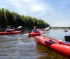 Two people are kayaking on a calm river surrounded by lush greenery on a sunny day