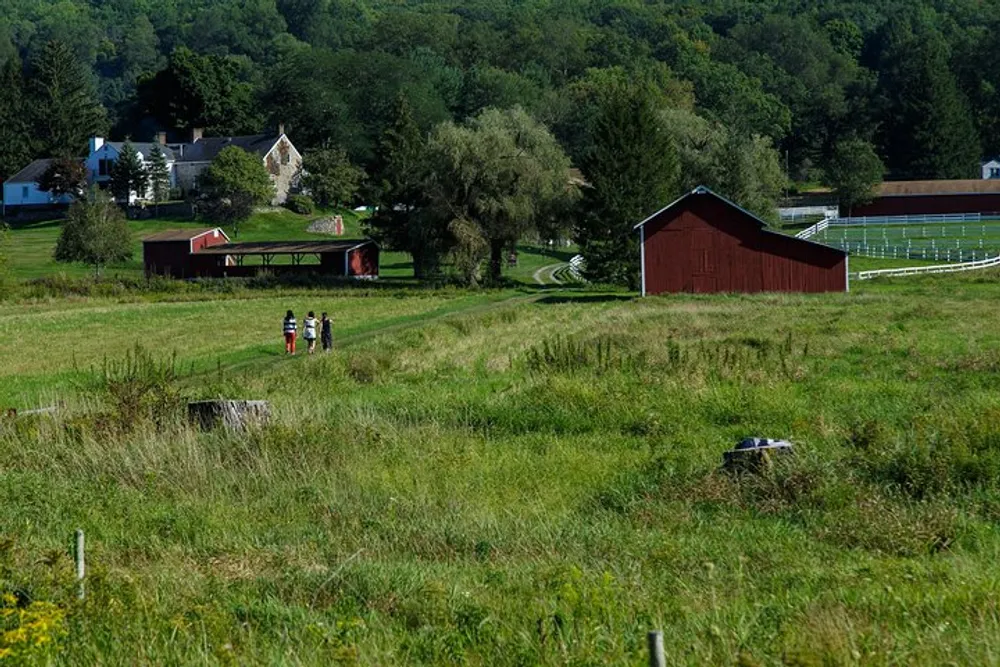 The image depicts a pastoral scene with a group of people walking through a lush green field with barn structures and trees in the background