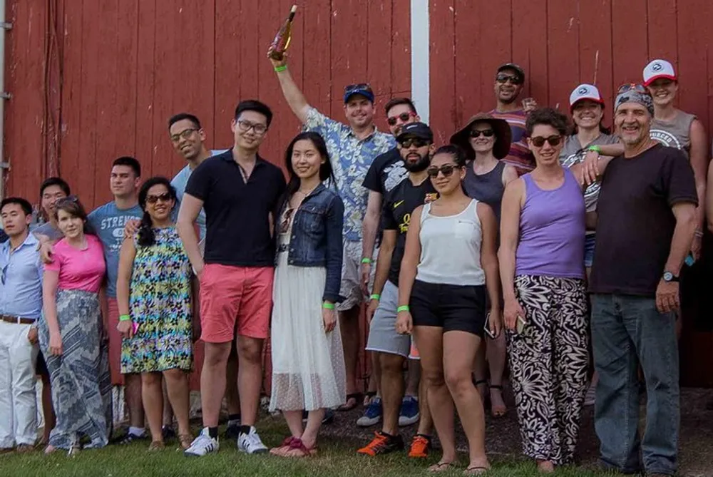 A diverse group of people are posing for a casual group photo outdoors with one person raising a bottle in celebration