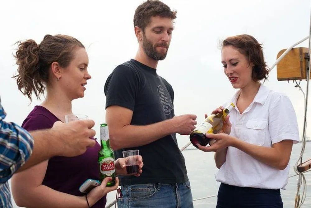 A group of friends is enjoying a social gathering on a boat with one person pouring wine while others hold drinks and converse