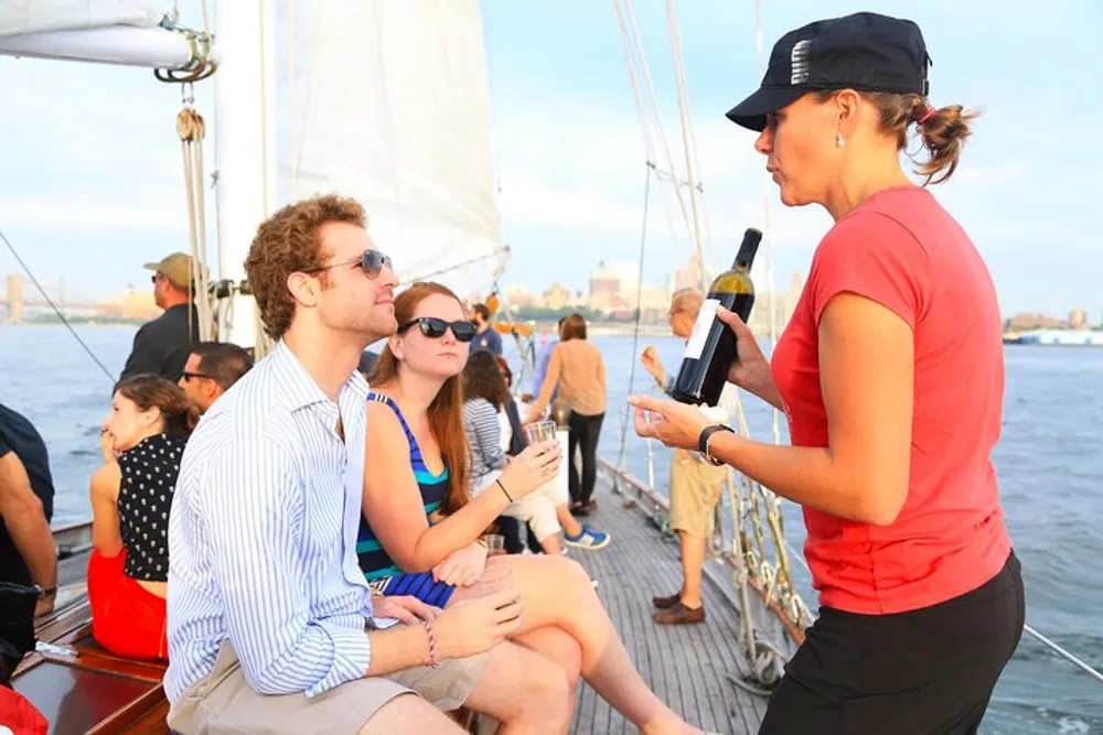 A staff member is presenting a bottle of wine to guests aboard a sailboat indicating a leisurely and social atmosphere