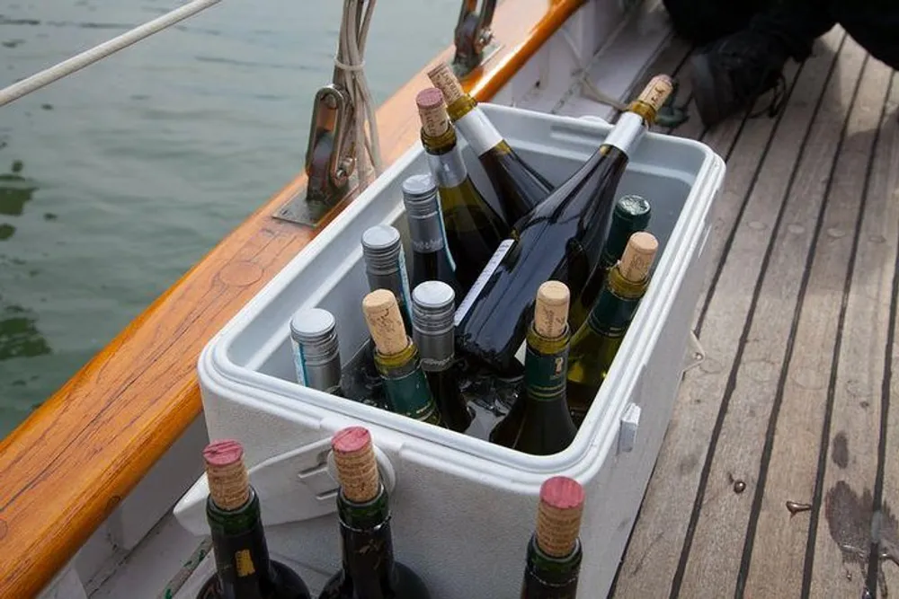 A white cooler is filled with various bottles of wine on the deck of a boat