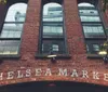 The image displays the exterior of the Chelsea Market with its name in large letters on a brick facade flanked by overhead lights
