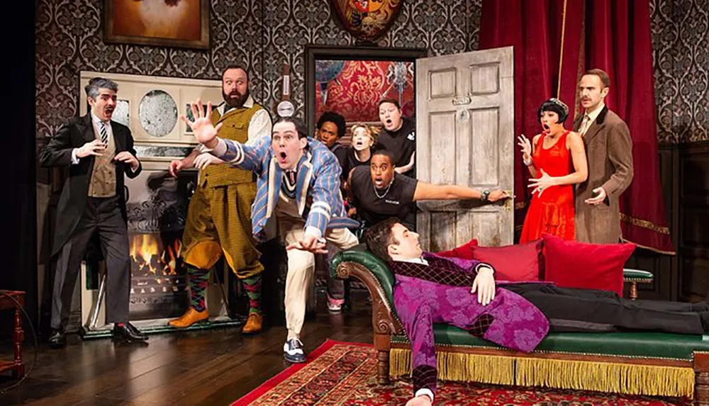 The image shows a dynamic and expressive theatrical scene with actors in various poses conveying a sense of surprise and chaos on an elaborately decorated stage