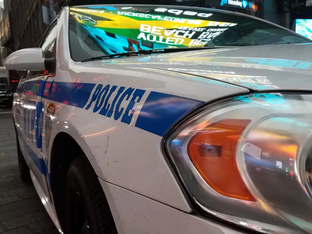The image shows a close-up of a white police car with blue and red stripes illuminated by the colorful lights of a city at night