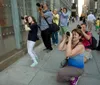 Several individuals are photographing something off-camera on a city sidewalk some using unique stances to capture their shot