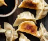 The image shows a plate of pan-fried dumplings next to a small bowl of dipping sauce