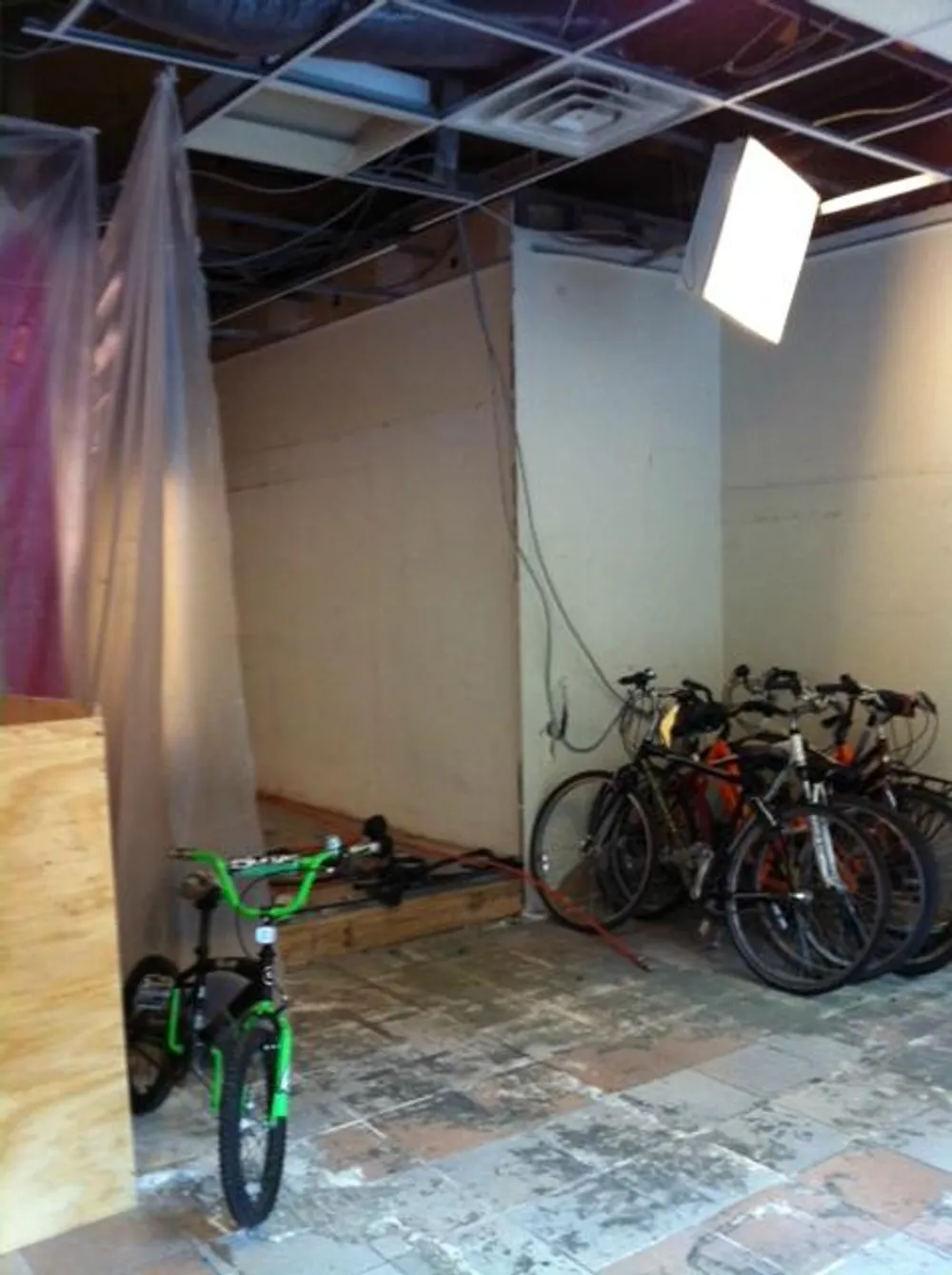 The image shows a cluttered and unfinished interior space with exposed ceiling infrastructure a group of bicycles parked on the right and a solitary green childrens bike in the foreground