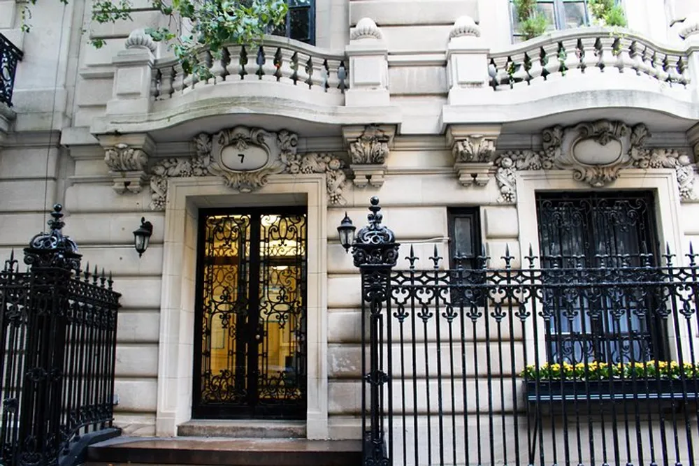 The image shows a classic grand entrance with ornate ironwork and intricate architectural details on the faade of an upscale urban building marked with the number 7